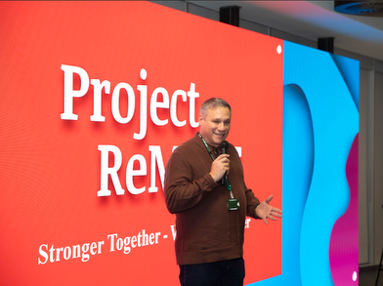 A speaker at a Project ReMAKE event in front of a Stronger Together backdrop